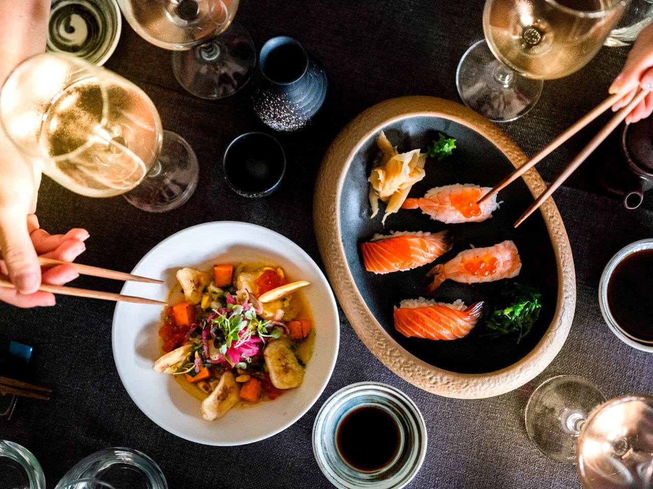 Et spisebord med sushi, en skål blandede grøntsager og vinglas.