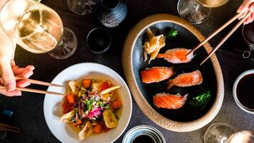 Et spisebord med sushi, en skål blandede grøntsager og vinglas.