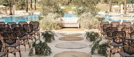 An outdoor wedding setup with a pool, wicker chairs, a sofa, and decorative plants.