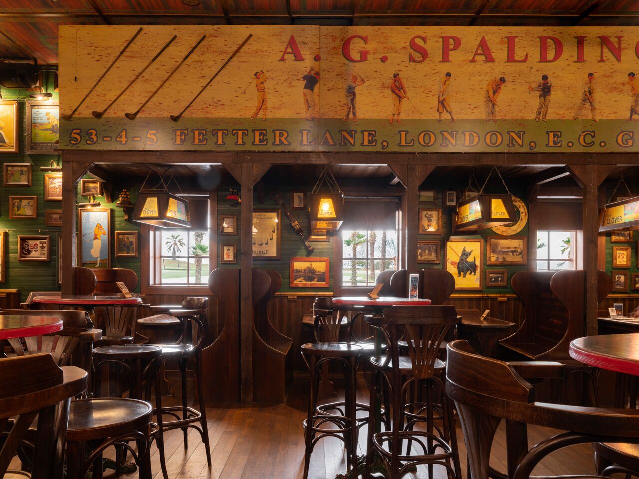 A traditional pub interior with wooden furniture, framed pictures on the walls, and a sign above the bar area.