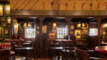 A traditional pub interior with wooden furniture, framed pictures on the walls, and a sign above the bar area.
