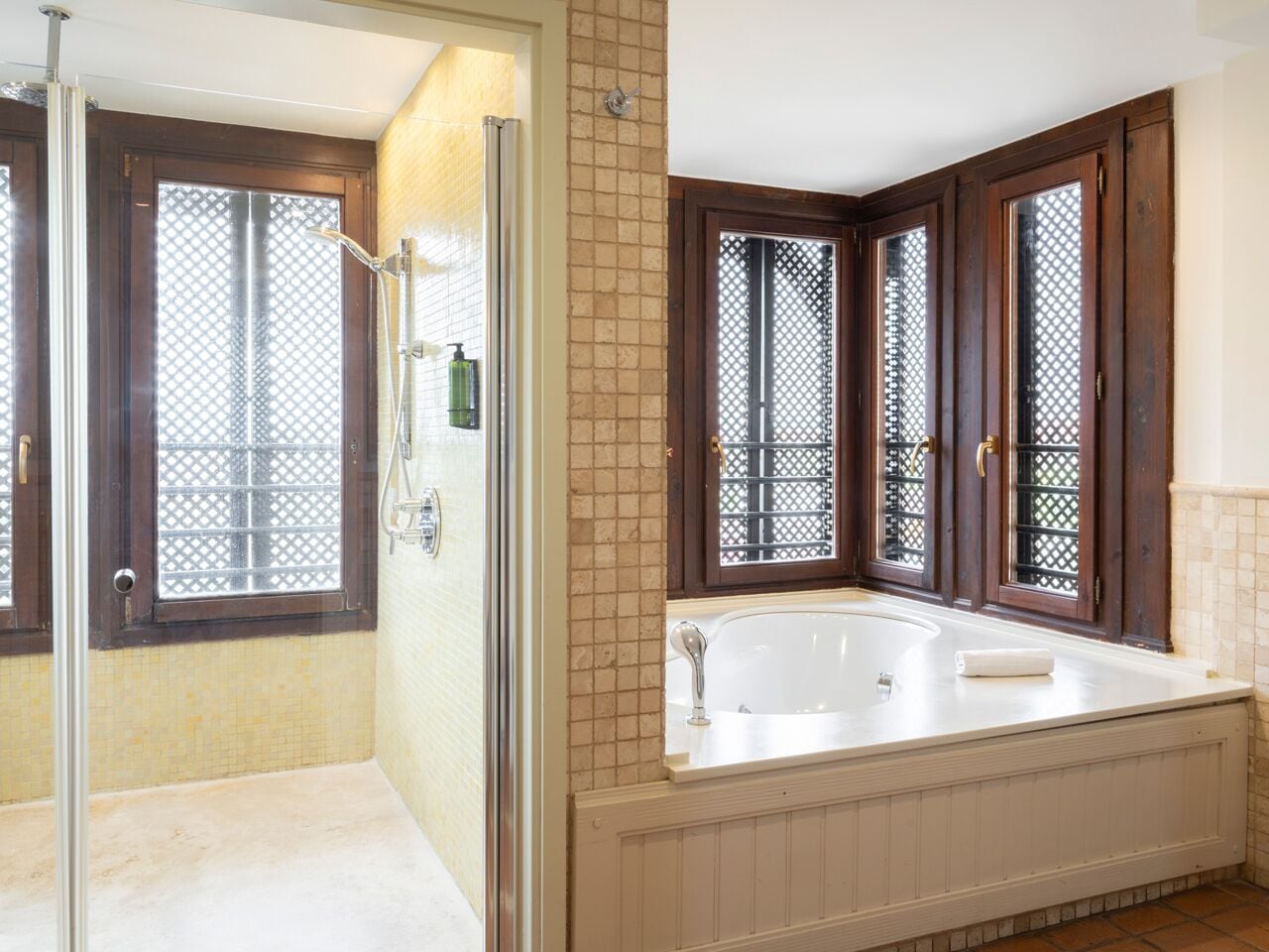 A bathroom with a walk-in shower, a bathtub, and a window with a lattice design.