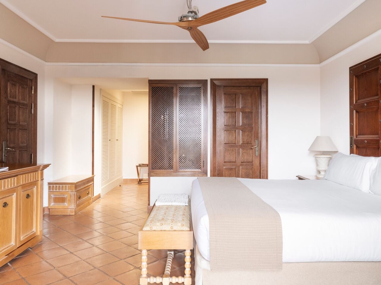 Une chambre à coucher comprenant un lit, une armoire en bois, un banc, un ventilateur de plafond et une fenêtre donnant sur un beau paysage.