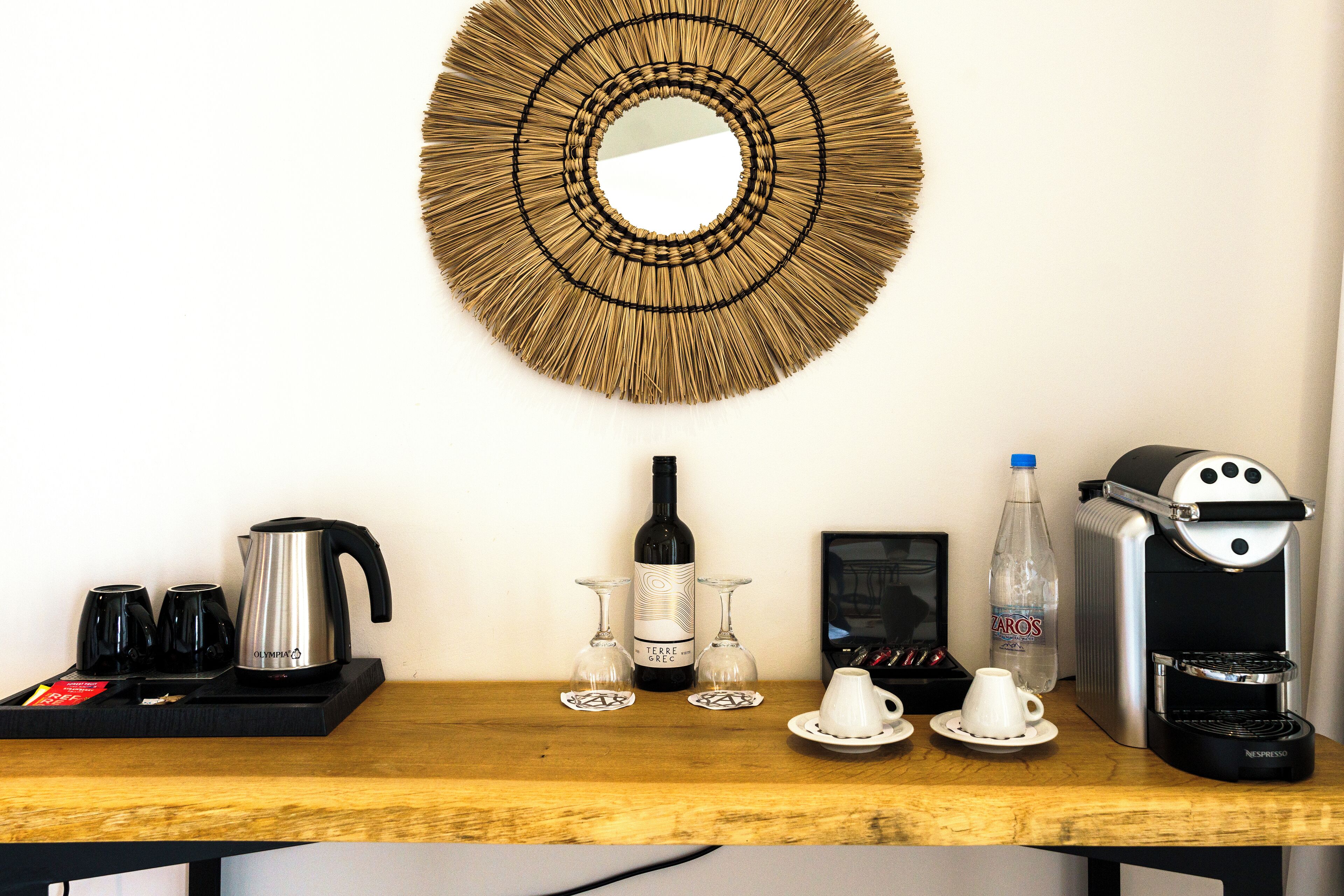 A breakfast setup with a coffee maker, wine bottle, glasses, and a water bottle on a wooden table.