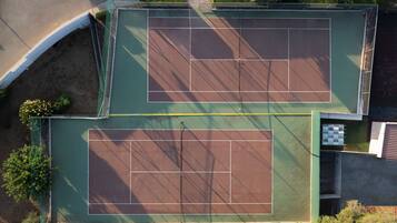 An aerial view of a tennis court complex with two courts, surrounded by greenery and adjacent to a road.