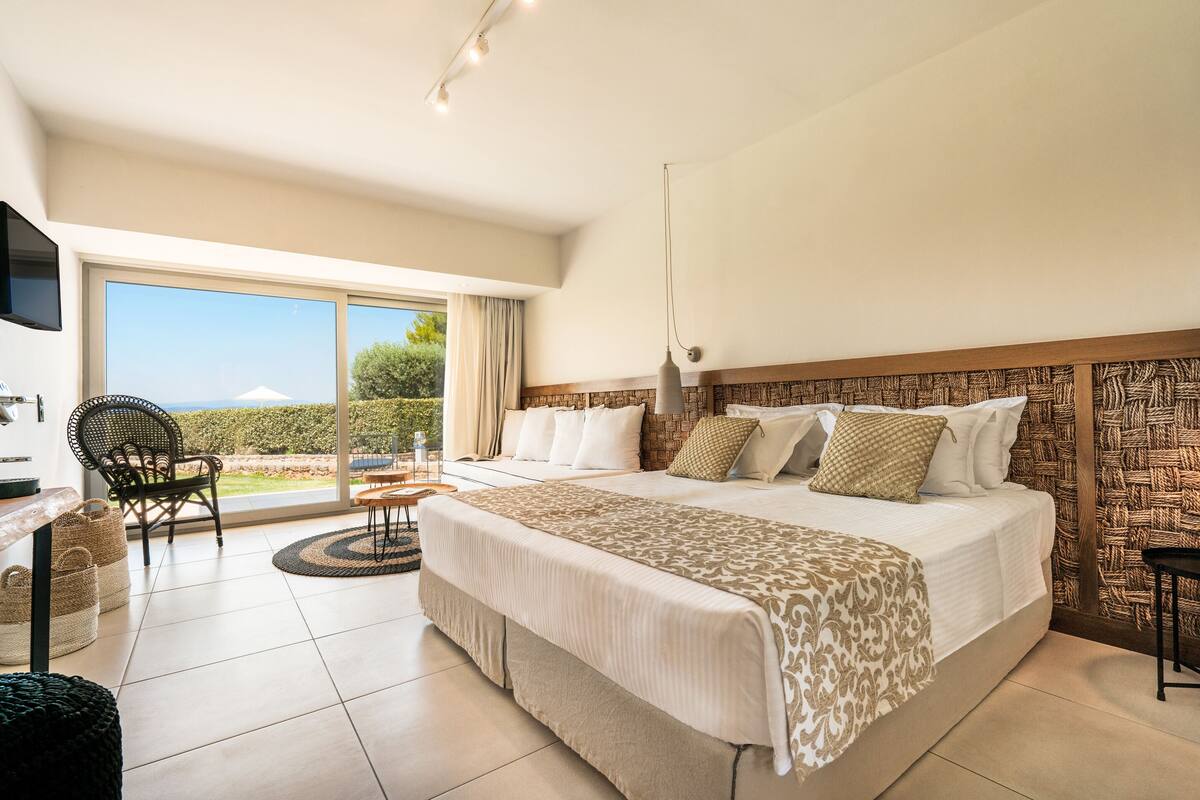 A spacious bedroom with a large bed, a television, a chair, and a view of the outdoors.
