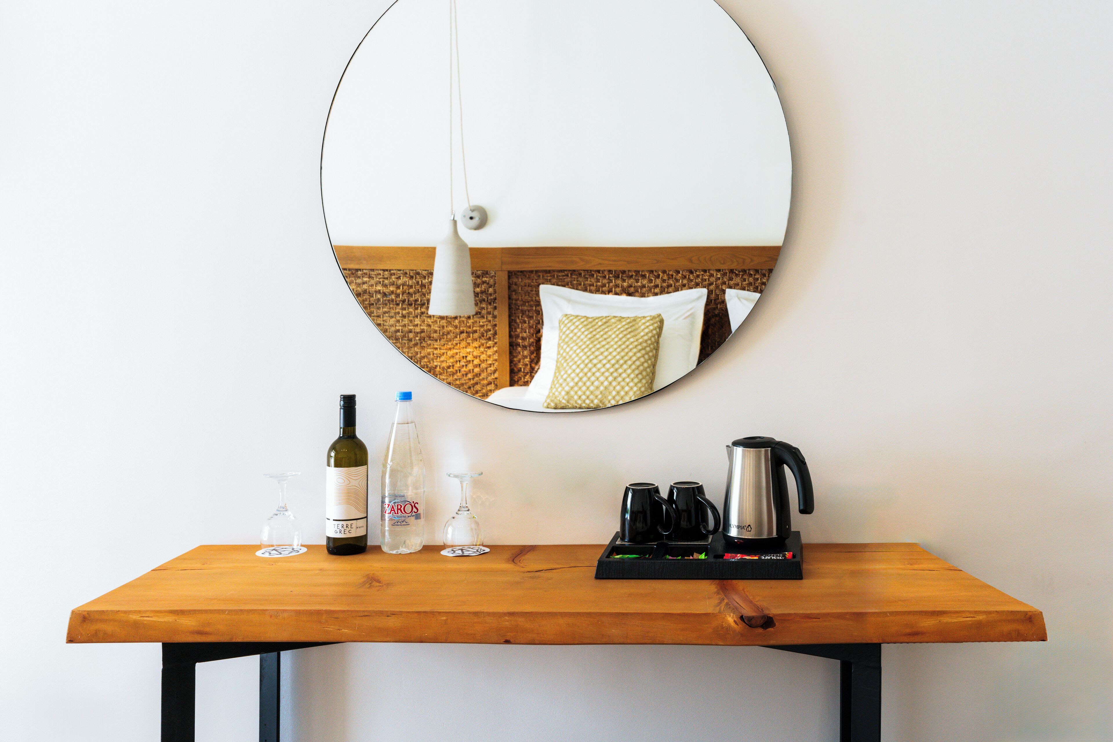 A wooden table with a wine bottle, glasses, a water bottle, and a coffee maker.