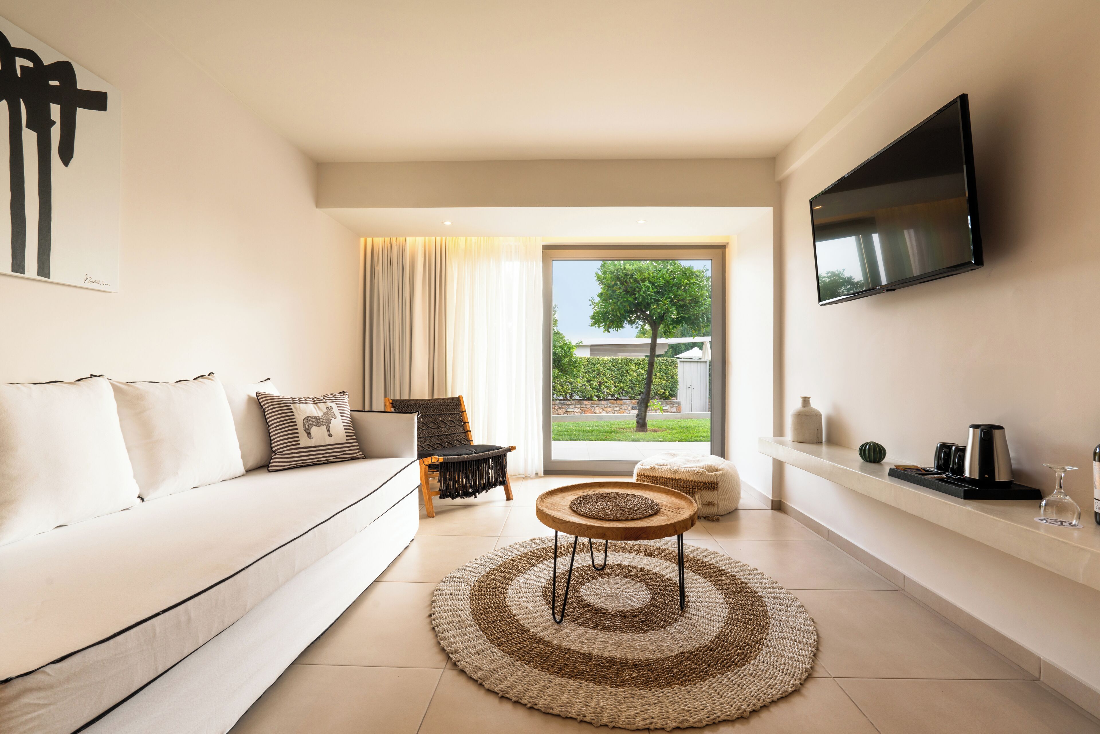 Una sala de estar moderna con un sofá, una mesa de centro, un televisor montado en la pared y vistas al exterior a través de una puerta de vidrio.
