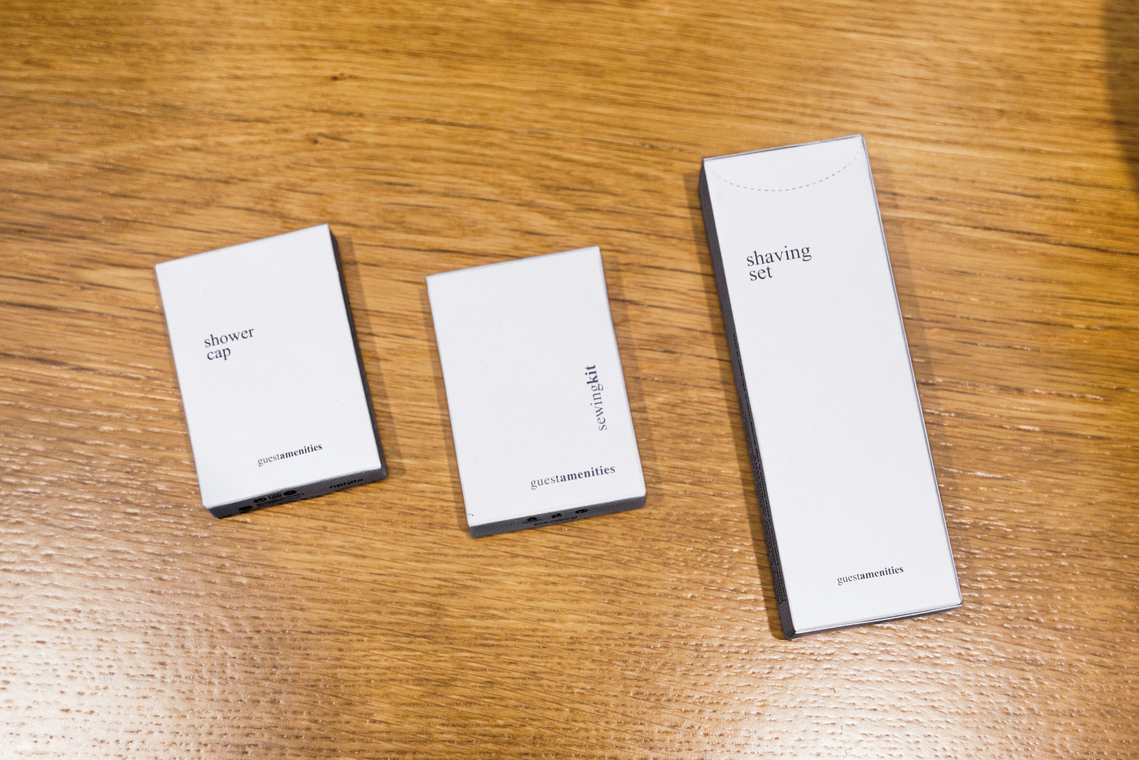 Three white boxes labeled "shower cap," "sewing kit," and "shaving set" from Guestamenities.