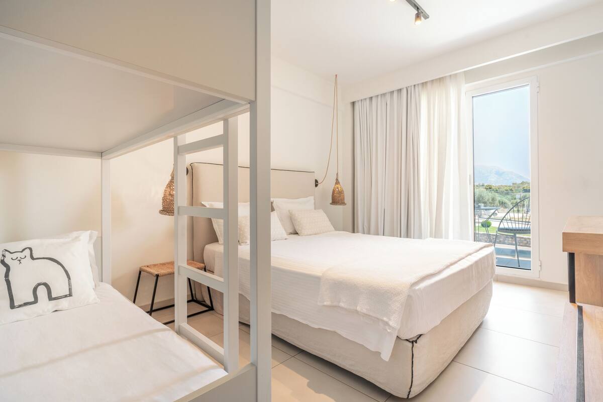 A modern hotel room with a large bed, a smaller bed, a seating area, and a balcony with a view.