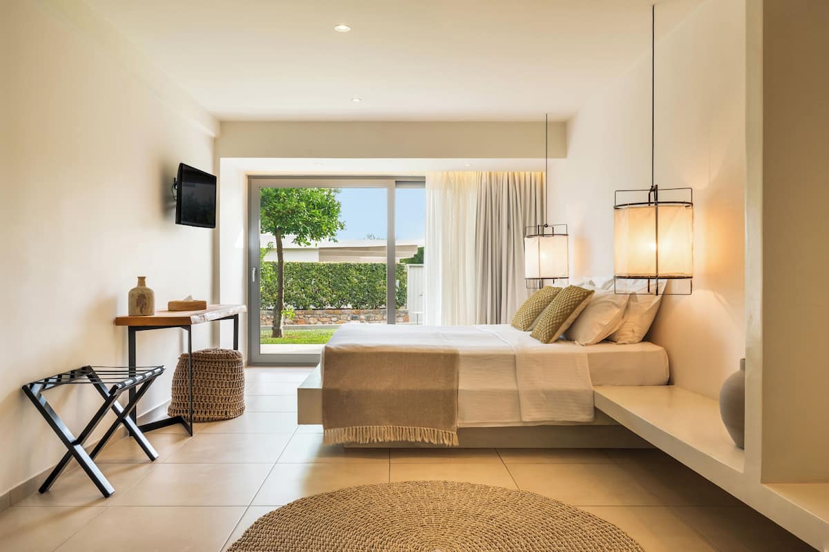 A modern bedroom with a bed, bedside tables, a flat-screen TV, and a view of the outdoors.