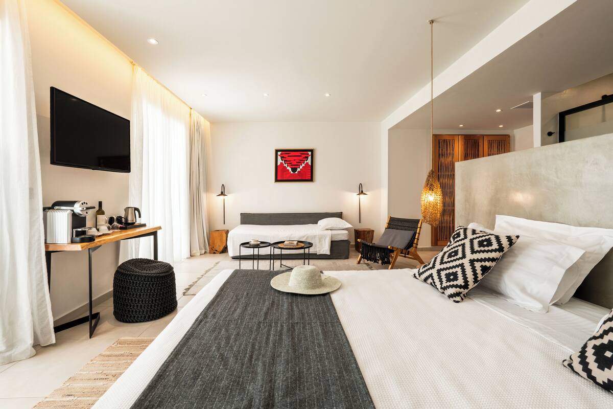 A modern hotel room with a large bed, a desk with a coffee maker, a TV, and a view of the city.