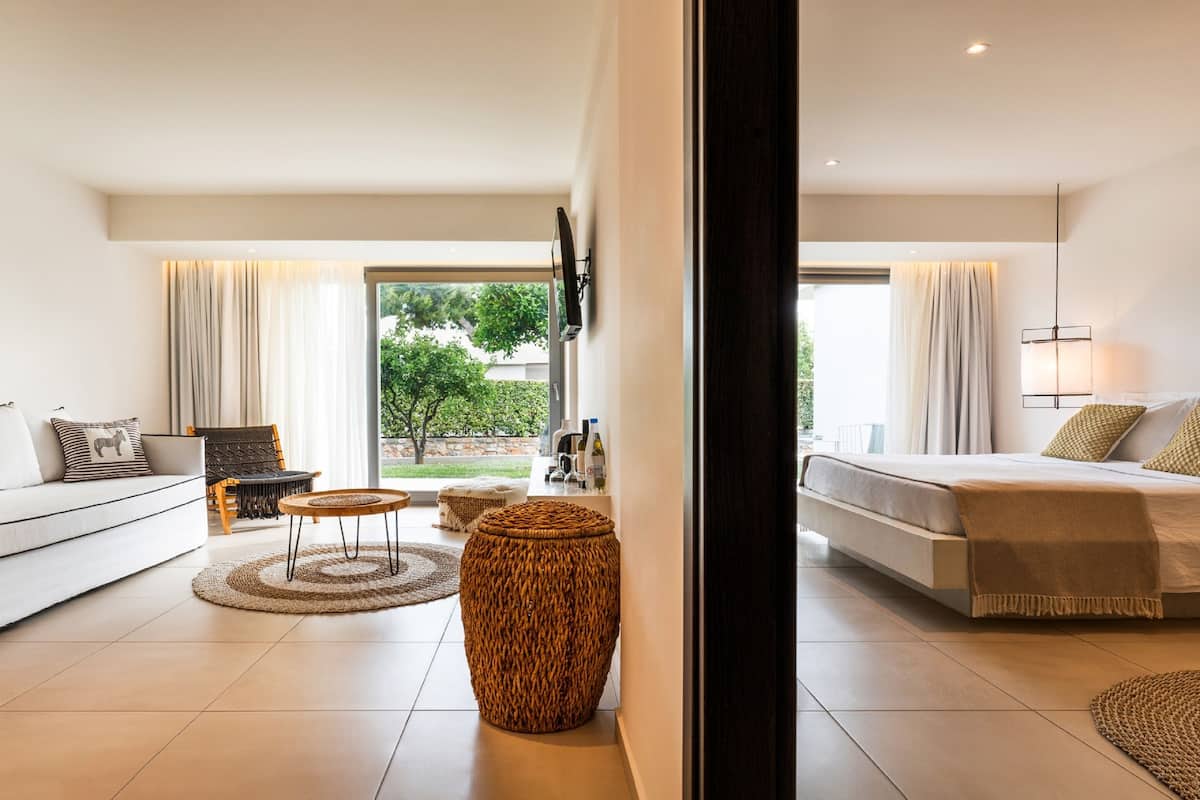 A modern hotel room with a sofa, a bed, a dining table, and a large window.