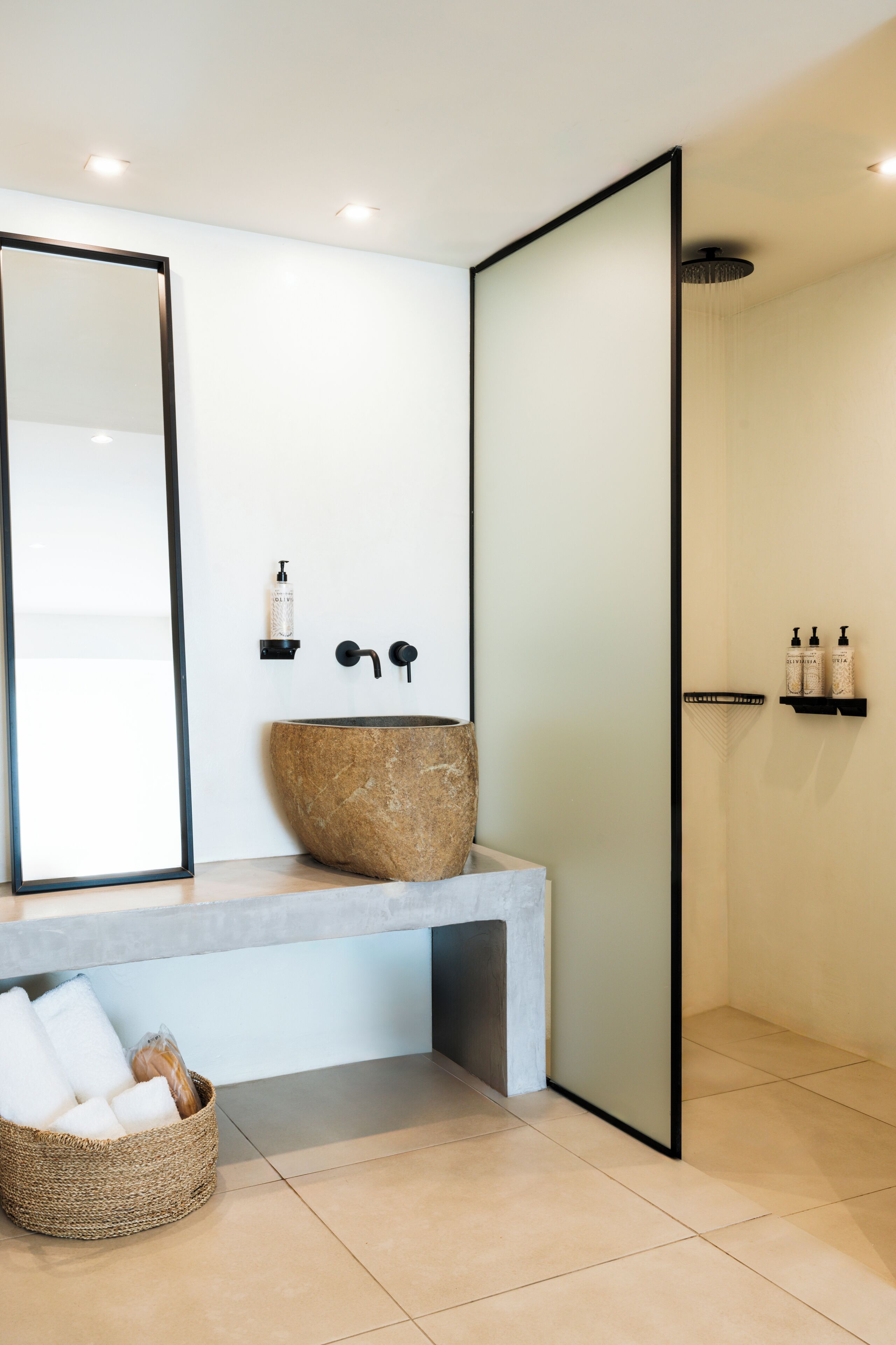 Un baño moderno con un espejo grande, un lavabo de piedra, un banco y una zona de ducha.