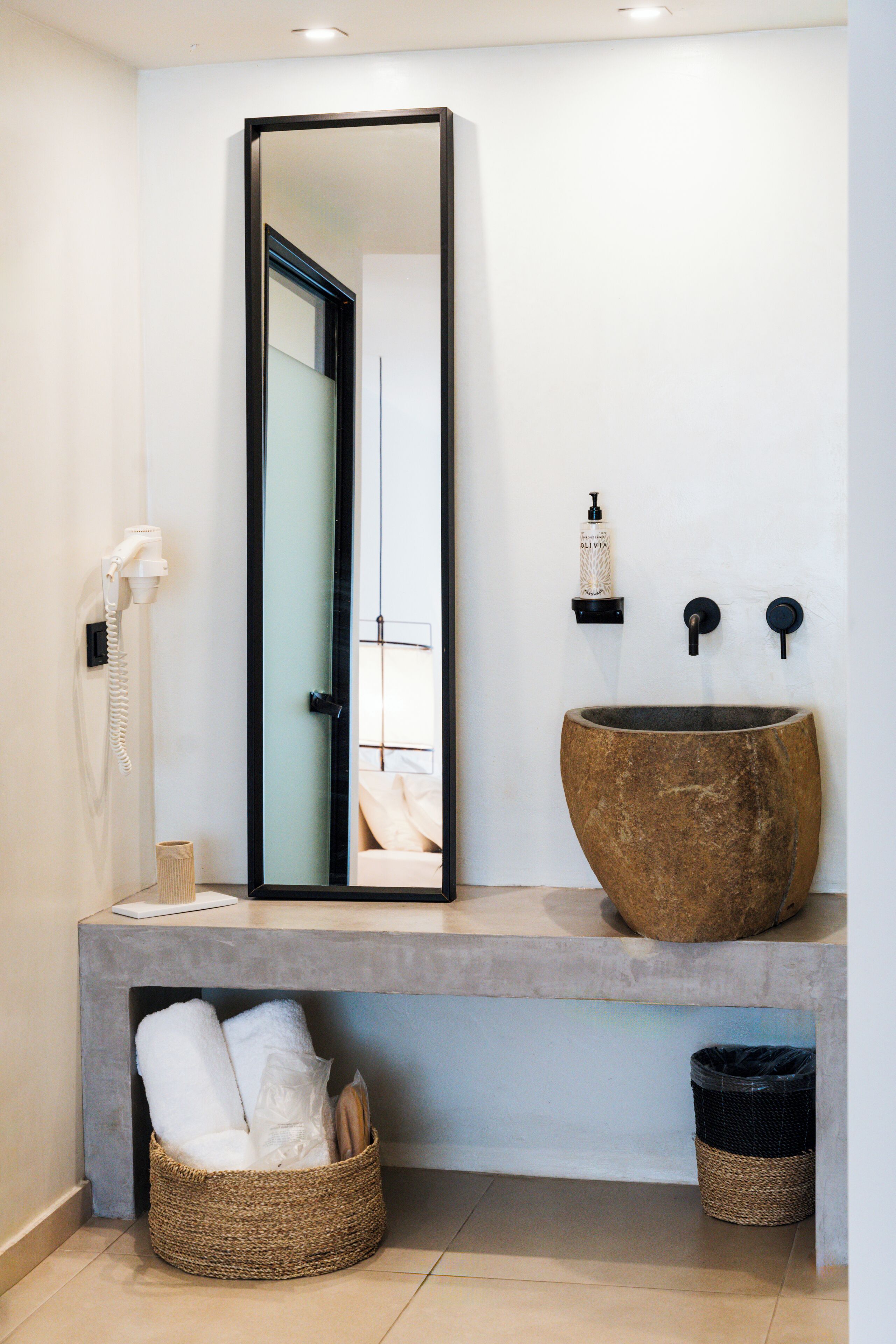 A bathroom with a large mirror, a stone sink, a towel rack, and a waste basket.