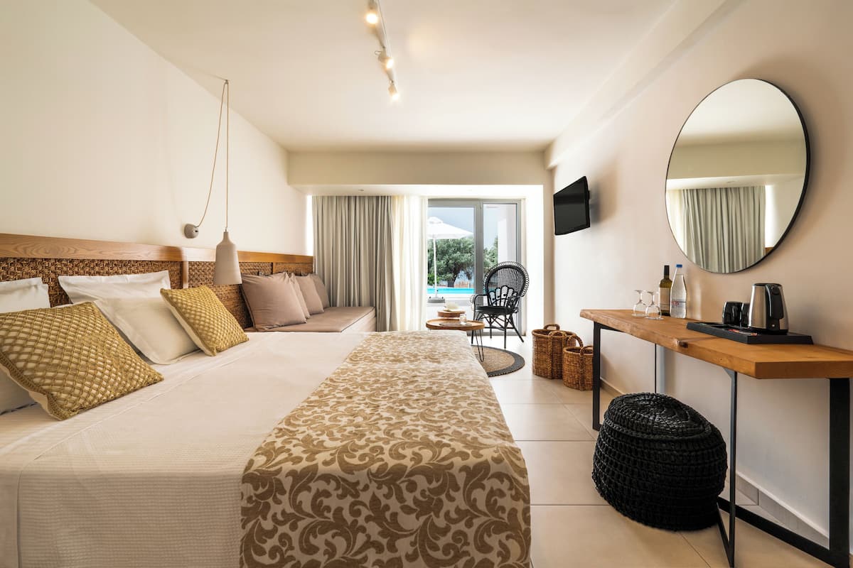 A hotel room with a large bed, a wooden side table, a TV, and a view of the outdoors.