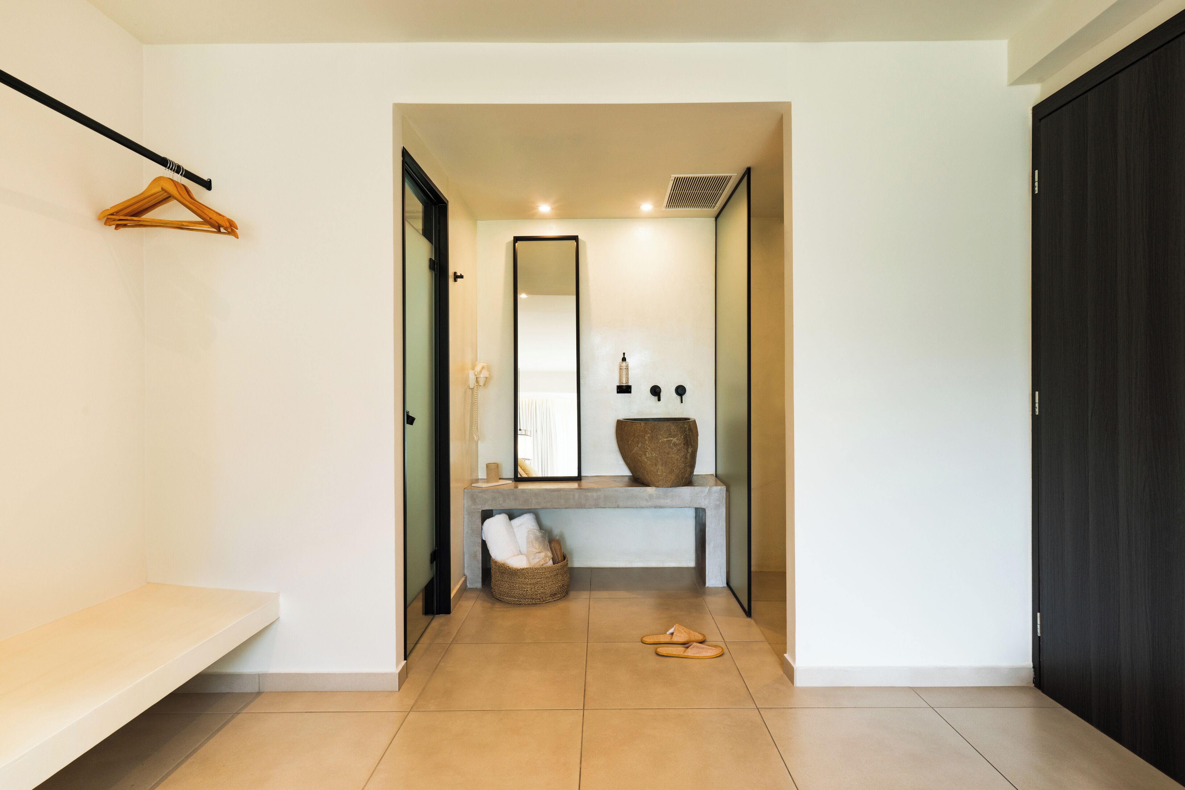 Un couloir avec un banc, un miroir, une console sur laquelle est posé un vase, et une porte.
