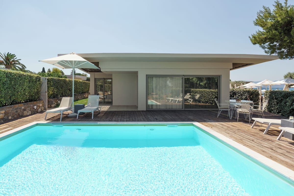 A modern outdoor pool area with a wooden deck, lounge chairs, and a covered seating area.
