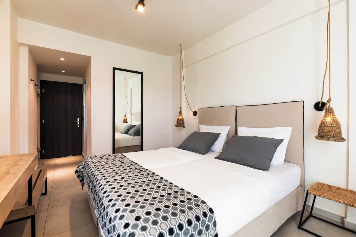 A modern bedroom with a large bed, a wooden desk, a mirror, and hanging lamps.