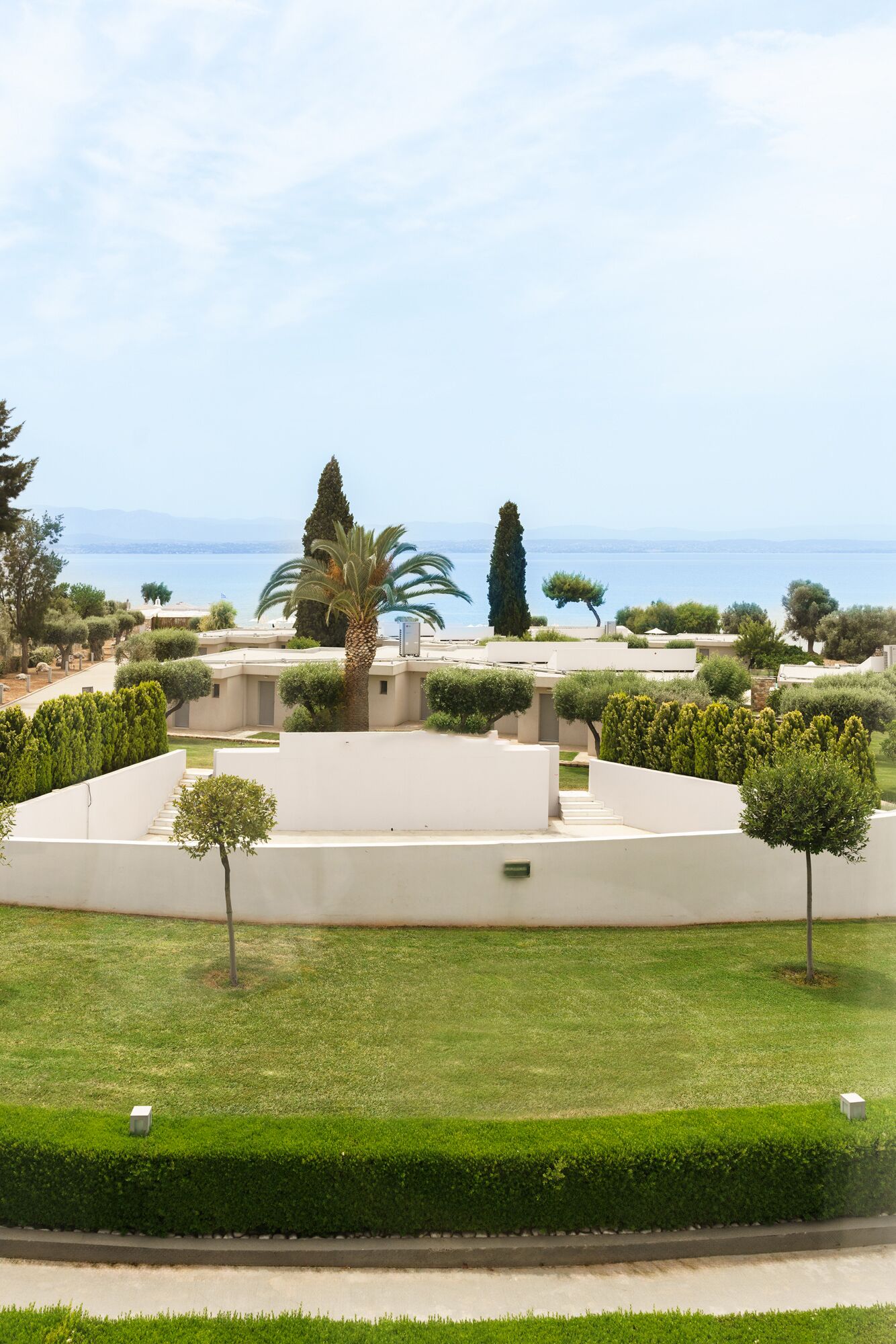 A landscaped garden with a palm tree, neatly trimmed hedges, and a view of the sea.