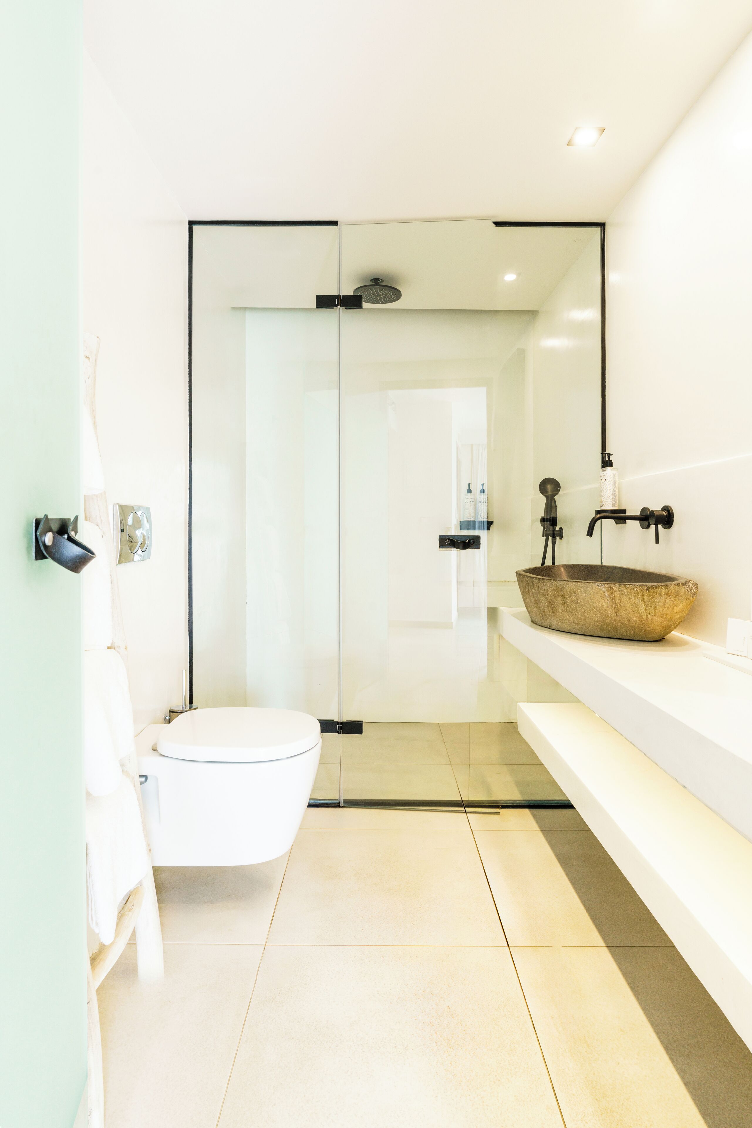Un baño moderno con ducha envuelta en vidrio, inodoro blanco y lavabo de madera sobre encimera blanca.
