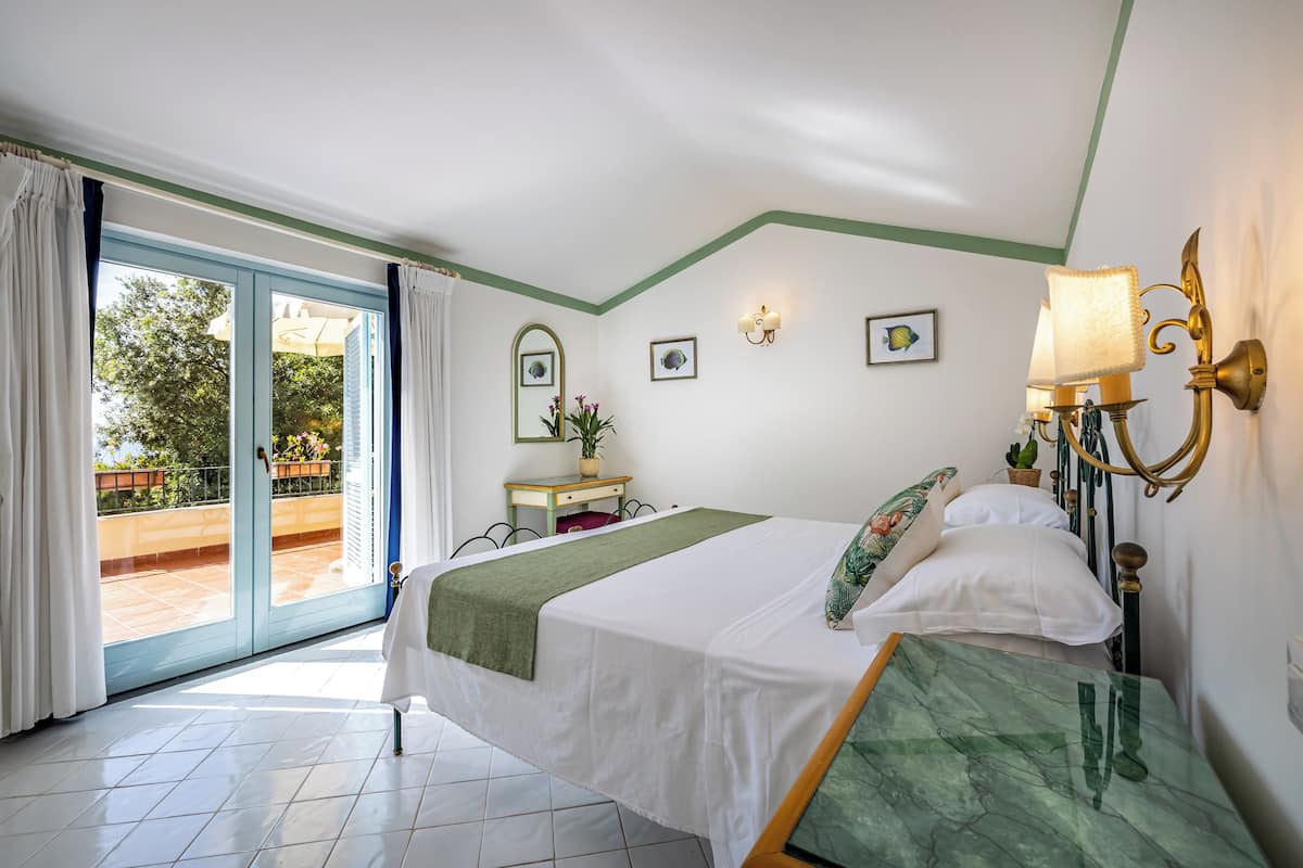 A hotel room with a bed, a desk, a chair, a window with curtains, and a view of the outside.