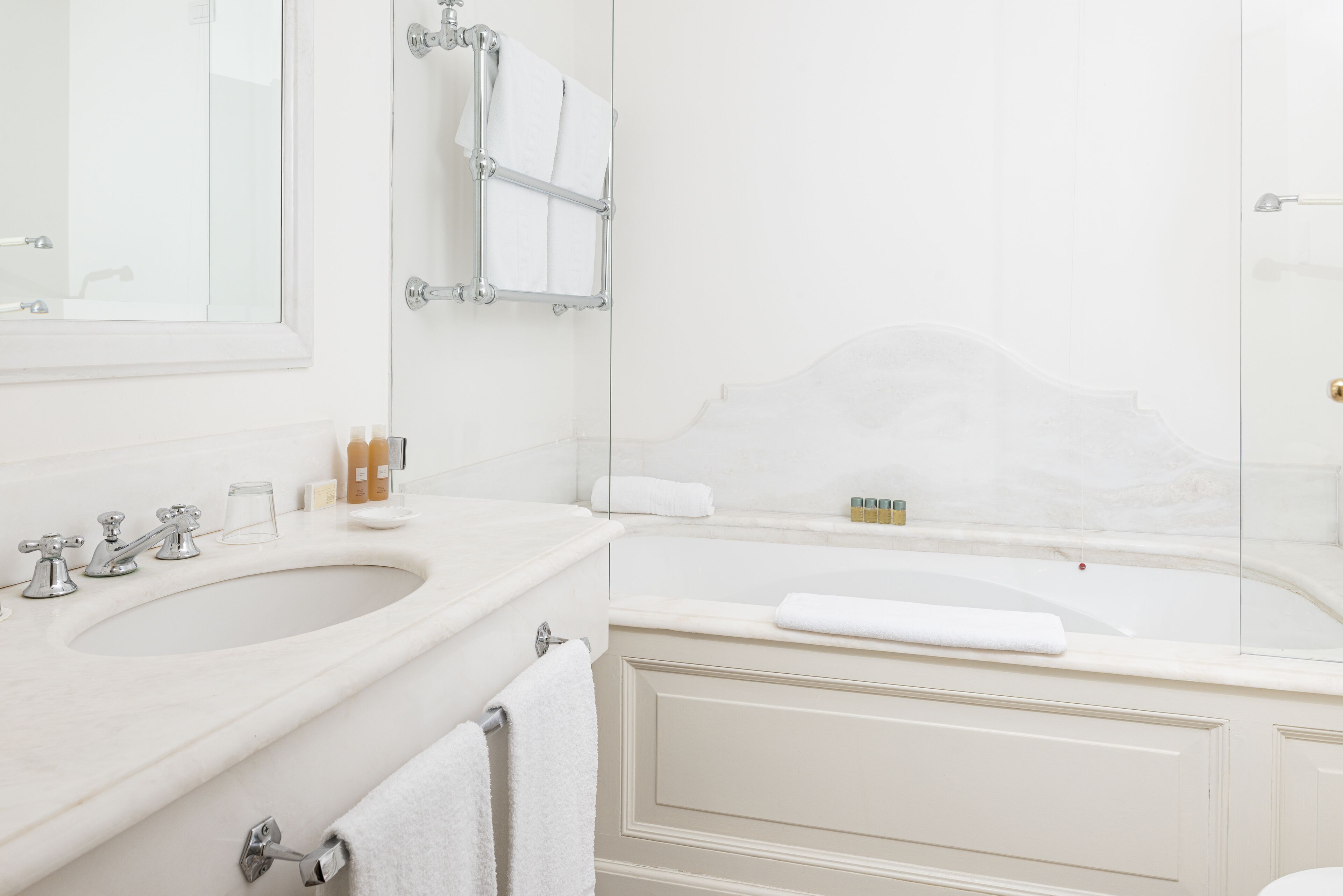 A bathroom with a sink, mirror, towel rack, and bathtub.