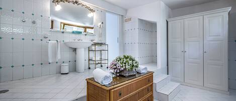 A modern bathroom with white tiles, a large mirror, a sink, and a wooden vanity with a basket of flowers.