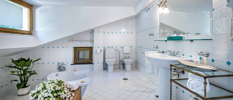 A modern bathroom with a large bathtub, a separate shower area, and a vanity with a glass shelf.