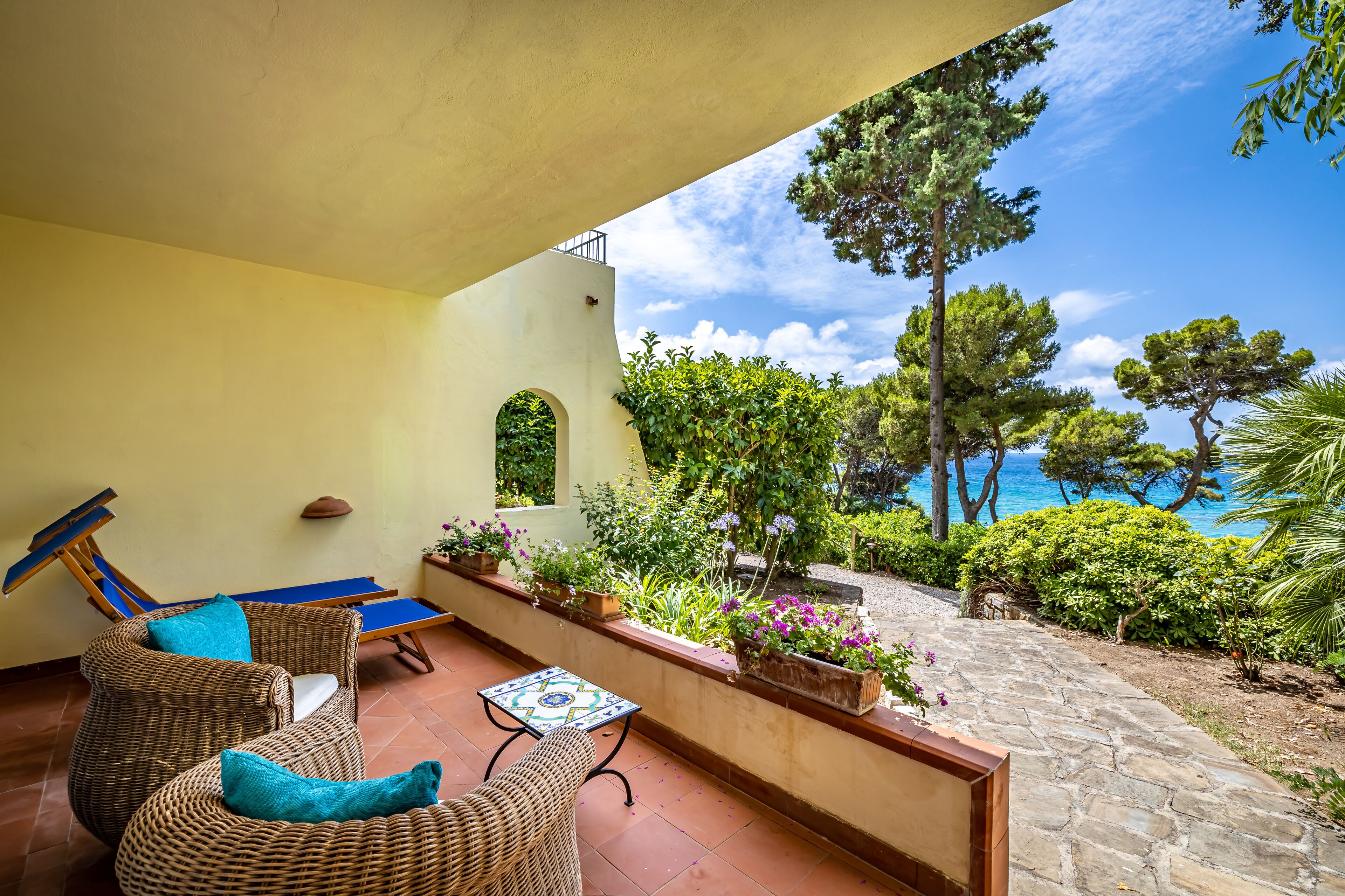 A balcony with wicker furniture, a table, and potted plants.