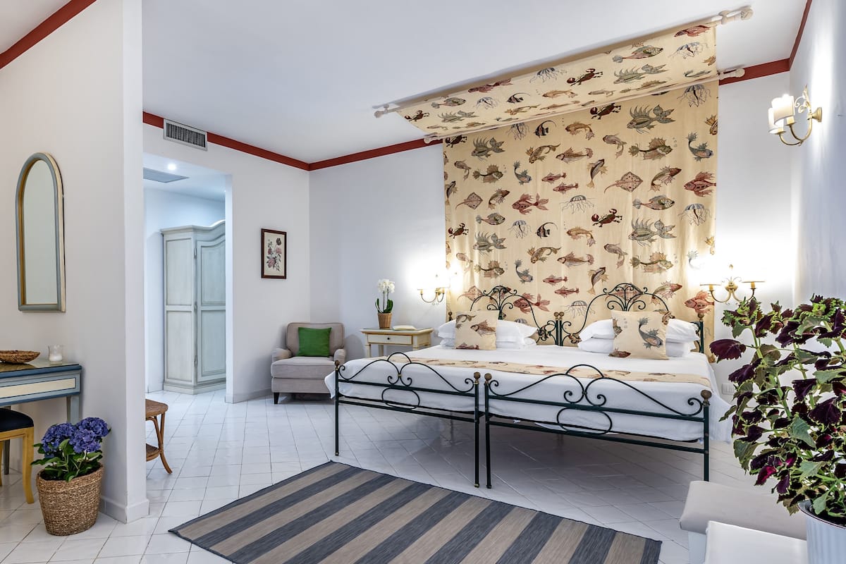 A bedroom with a bed, a nightstand, a chair, a dresser, a mirror, and a potted plant.