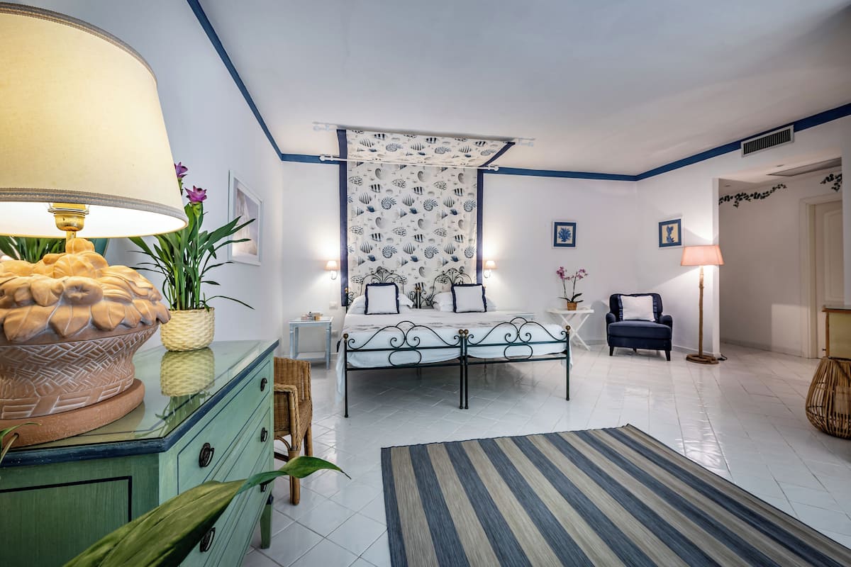 A bedroom with a bed, bedside tables, a lamp, a decorative plant, and a patterned curtain.