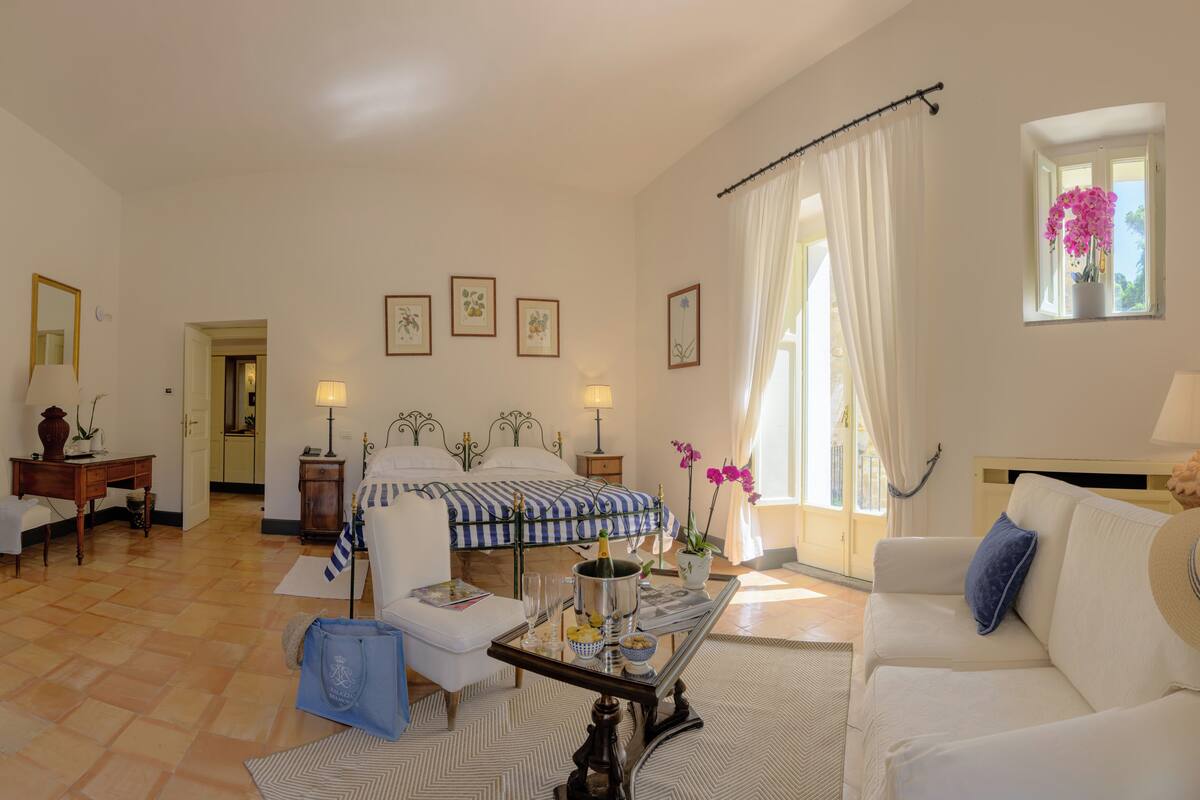 A well-lit room with a bed, a sofa, a dining table, and a window with curtains.