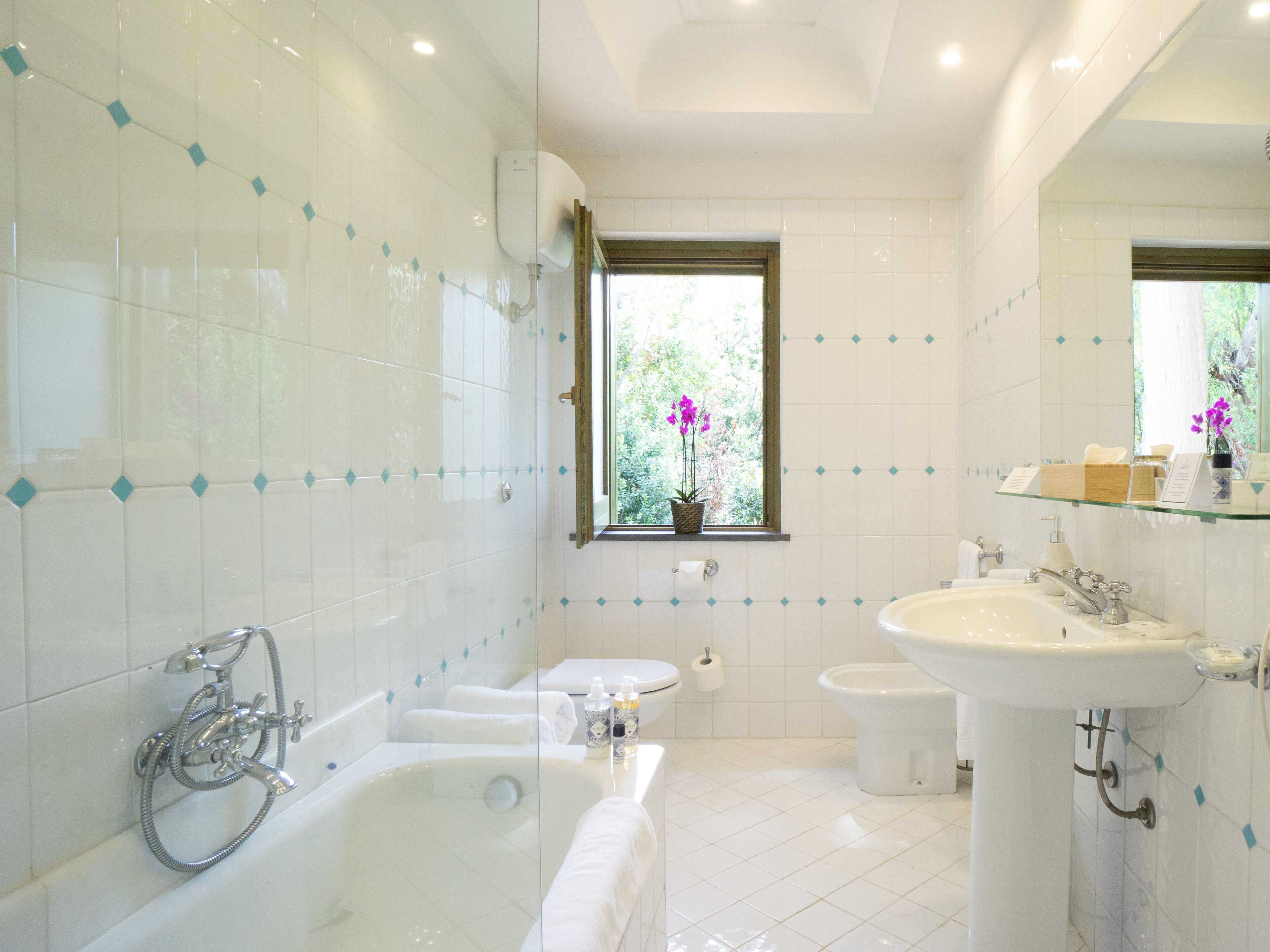 A modern bathroom with a bathtub, a sink, and a toilet. There is a window with a view of greenery outside.