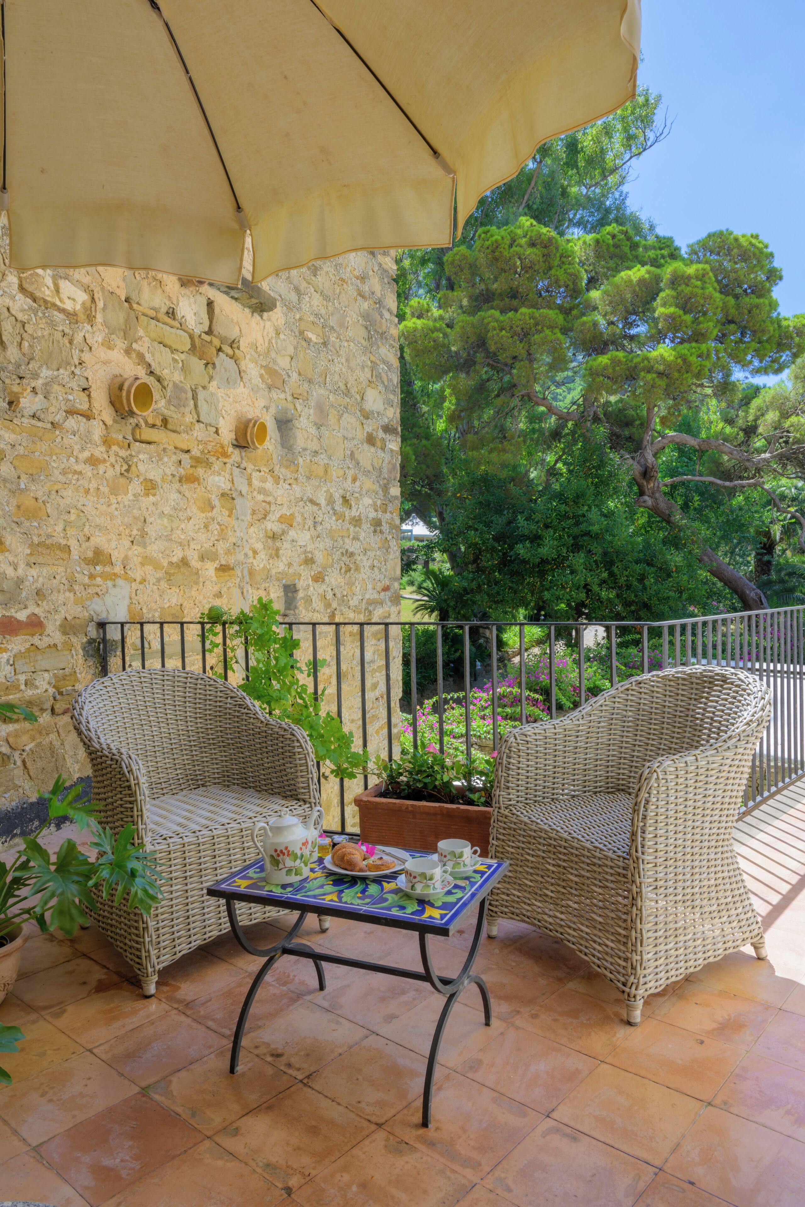 Un patio con sedie in vimini, un tavolo con tovaglia fiorata e un muro in pietra.