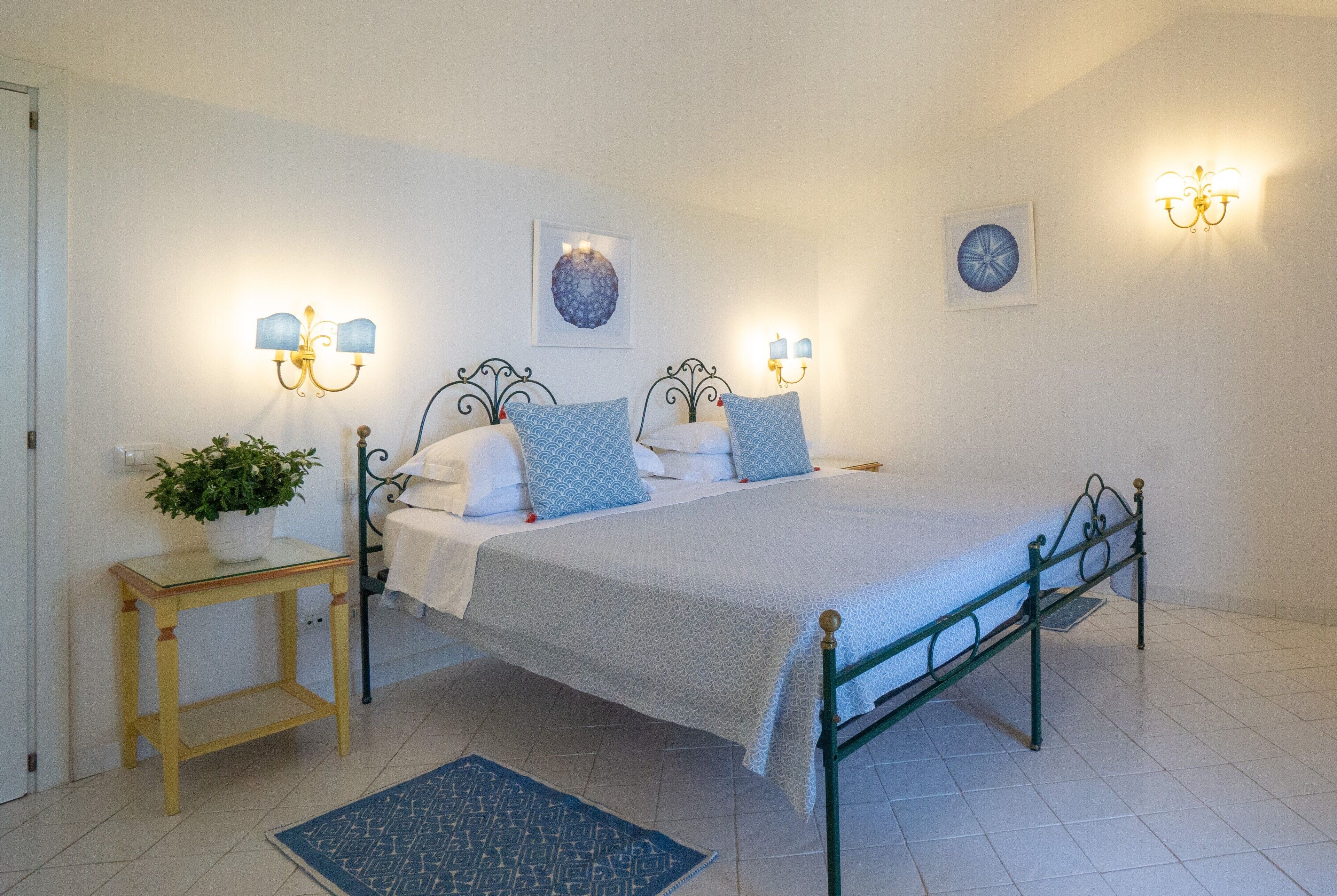 Ein ordentlich eingerichtetes Schlafzimmer mit einem Bett, Nachttischen, Wandlampen und einer Topfpflanze.