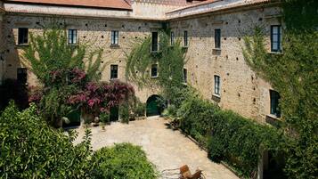 Un cortile con pavimento in pietra, una carrozza e vegetazione lussureggiante.