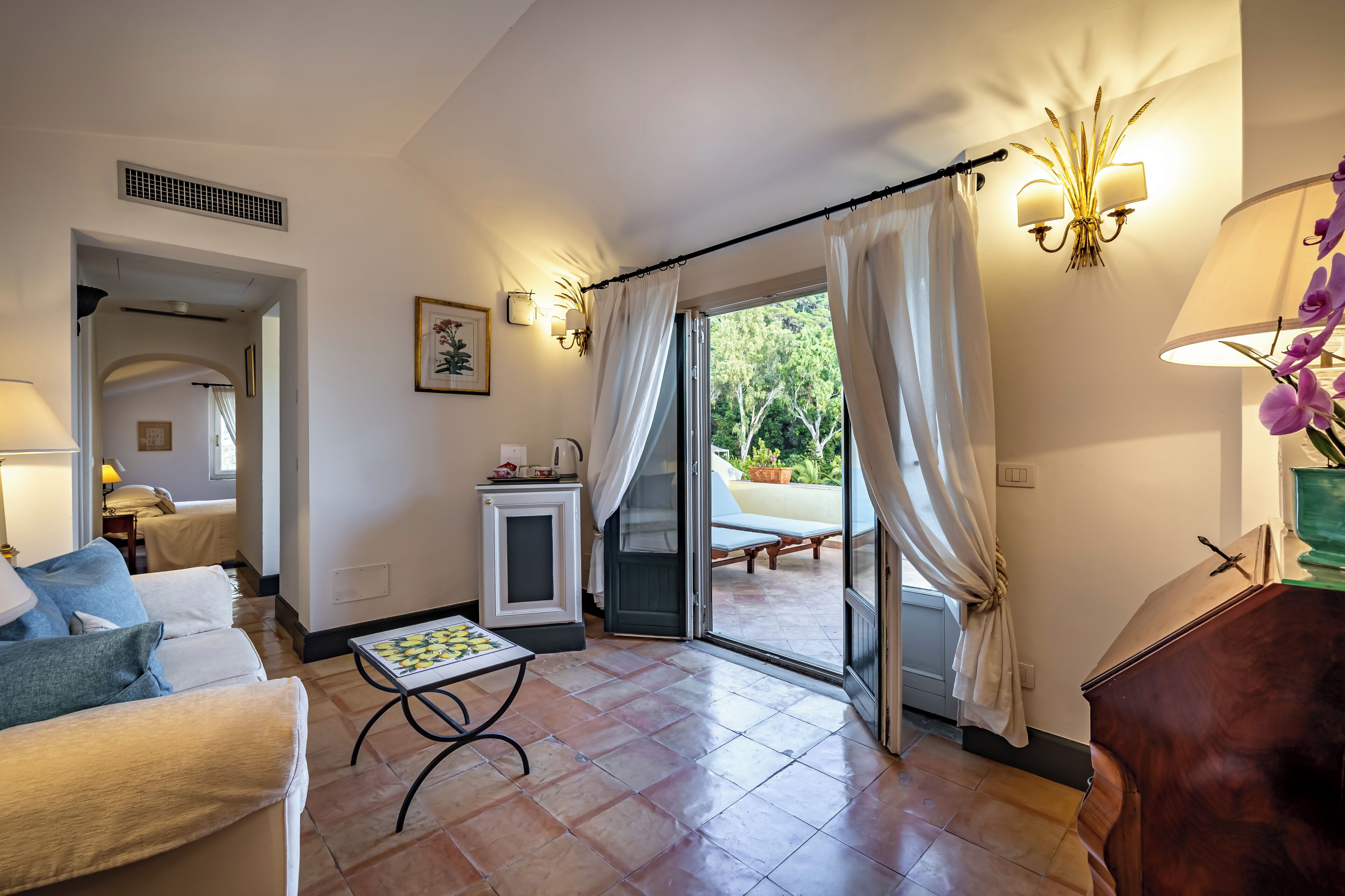 A spacious living room with a sofa, a small table, and a view of the outdoors through a sliding glass door.