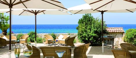 A seaside patio with wicker furniture and large umbrellas, overlooking the ocean.