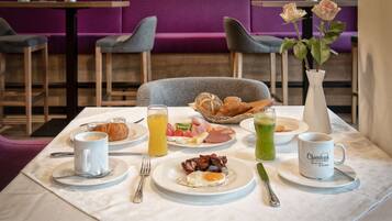 Mesa de desayuno preparada con croissants, huevos, tocino y jugo, en un comedor moderno con detalles morados.