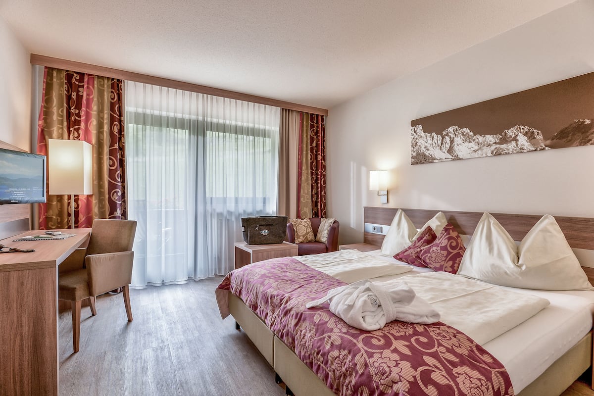 A hotel room with a bed, a desk, a chair, a TV, and a window with curtains.