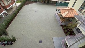 Une cour dallée de béton, entourée d’immeubles dotés de balcons et d’un espace de repos abrité.