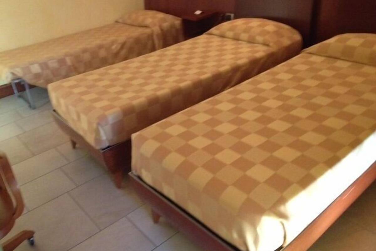 A hotel room with two single beds, a wooden headboard, a nightstand, and a chair.
