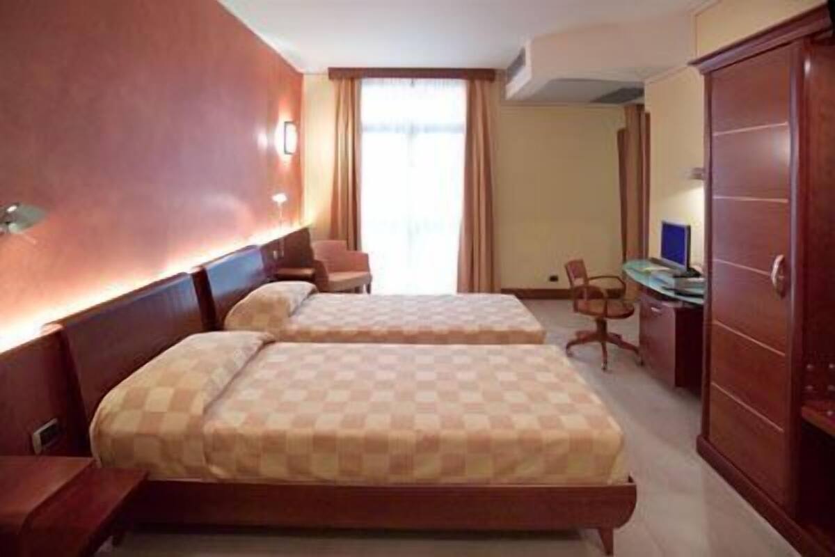 A hotel room with two beds, a desk, a chair, and a wardrobe.