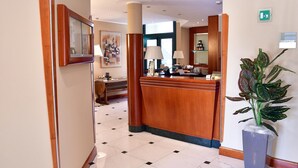 Un espace d’accueil d’hôtel comprenant un comptoir de réception en bois, une grande plante en pot et un bureau d’accueil.
