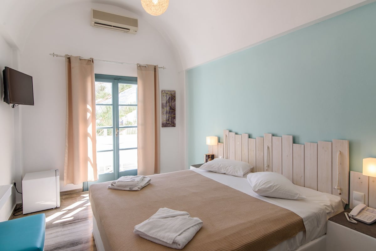 A hotel room with a large bed, a flat-screen TV, a desk with a chair, and a window with curtains.
