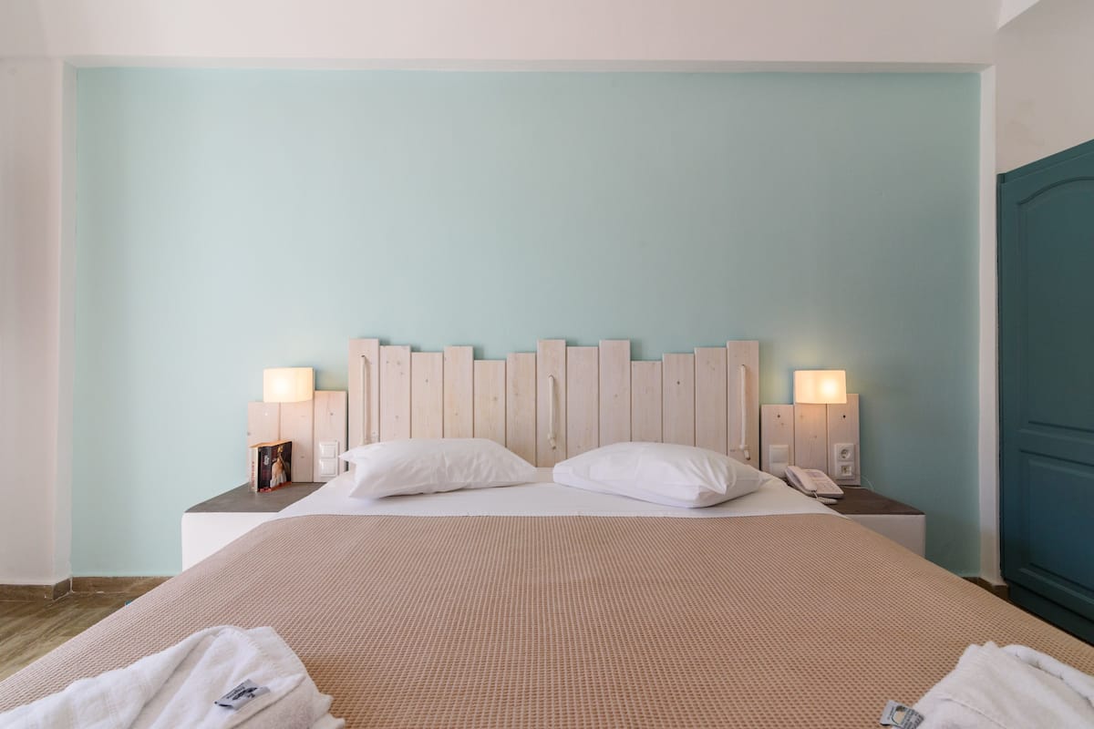 A neatly made bed with a headboard, two bedside tables with lamps, and a blue door.