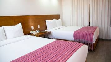 Habitación de hotel con dos camas, cabecero de madera, ropa de cama blanca, teléfono y ventana con cortinas.