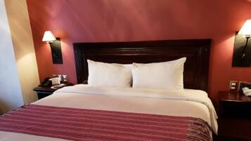 A hotel room with a large bed, two bedside lamps, and a nightstand with a lamp.