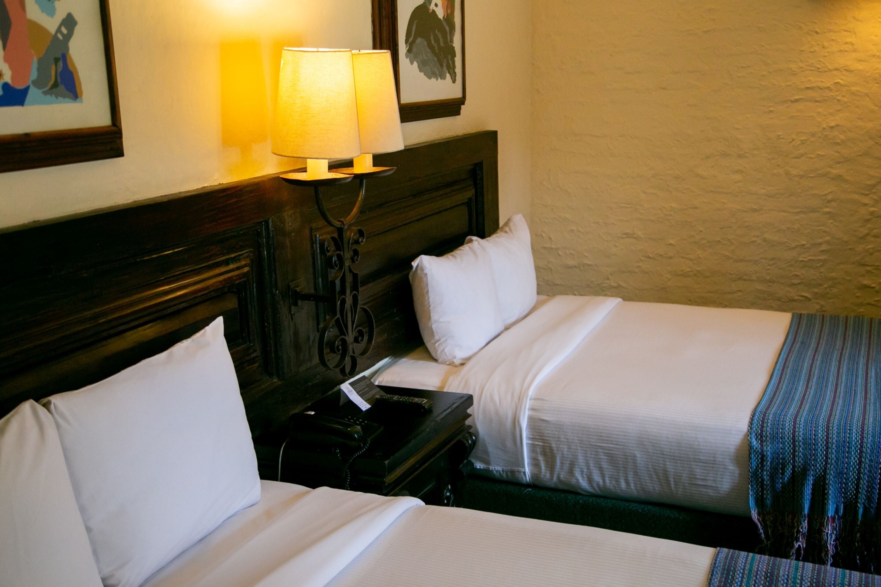 A hotel room with two beds, a nightstand, a lamp, and a framed picture on the wall.